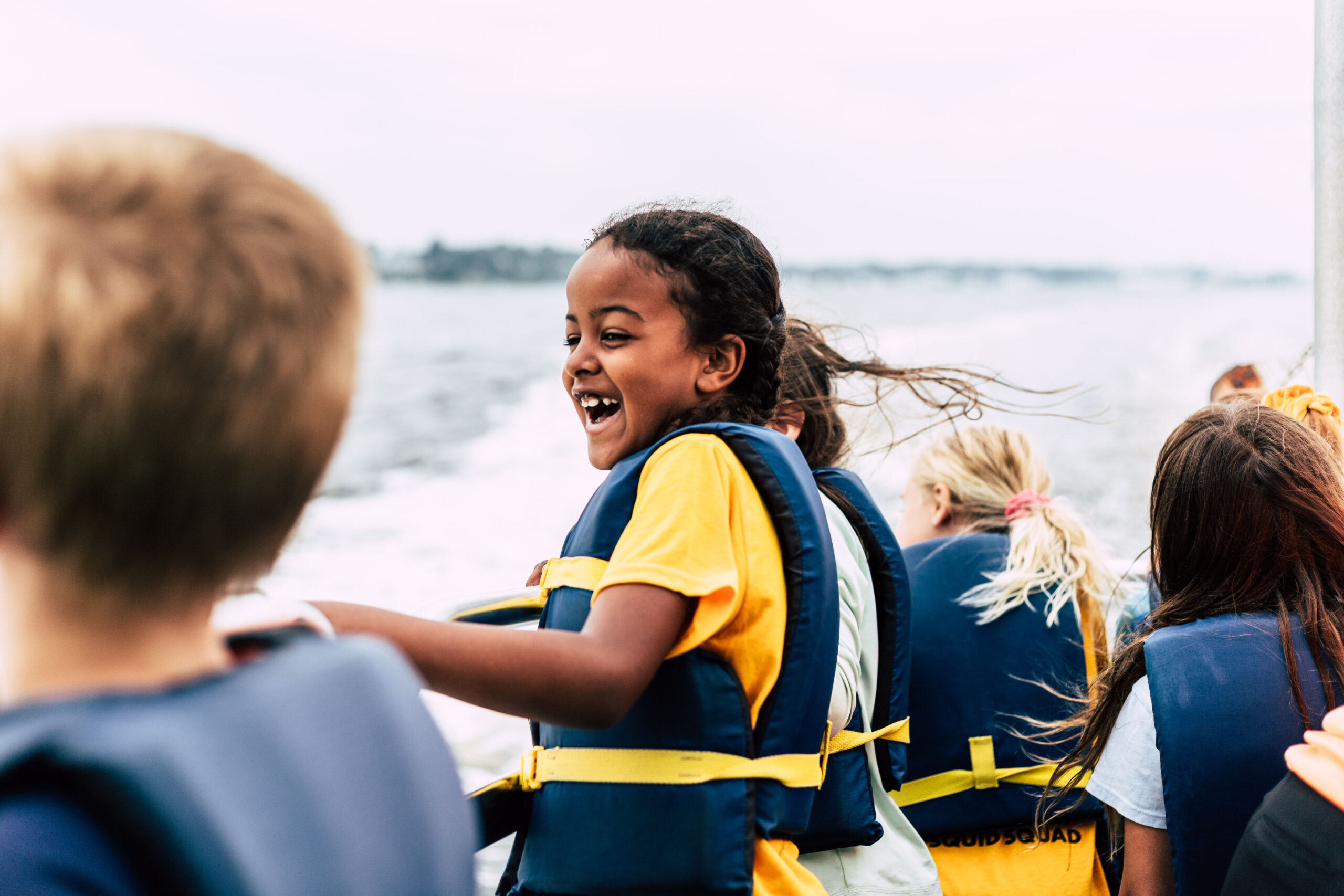 A BayCamper sporting a blue life jacket delights in a boat ride on Narragansett Bay in Summer 2023.