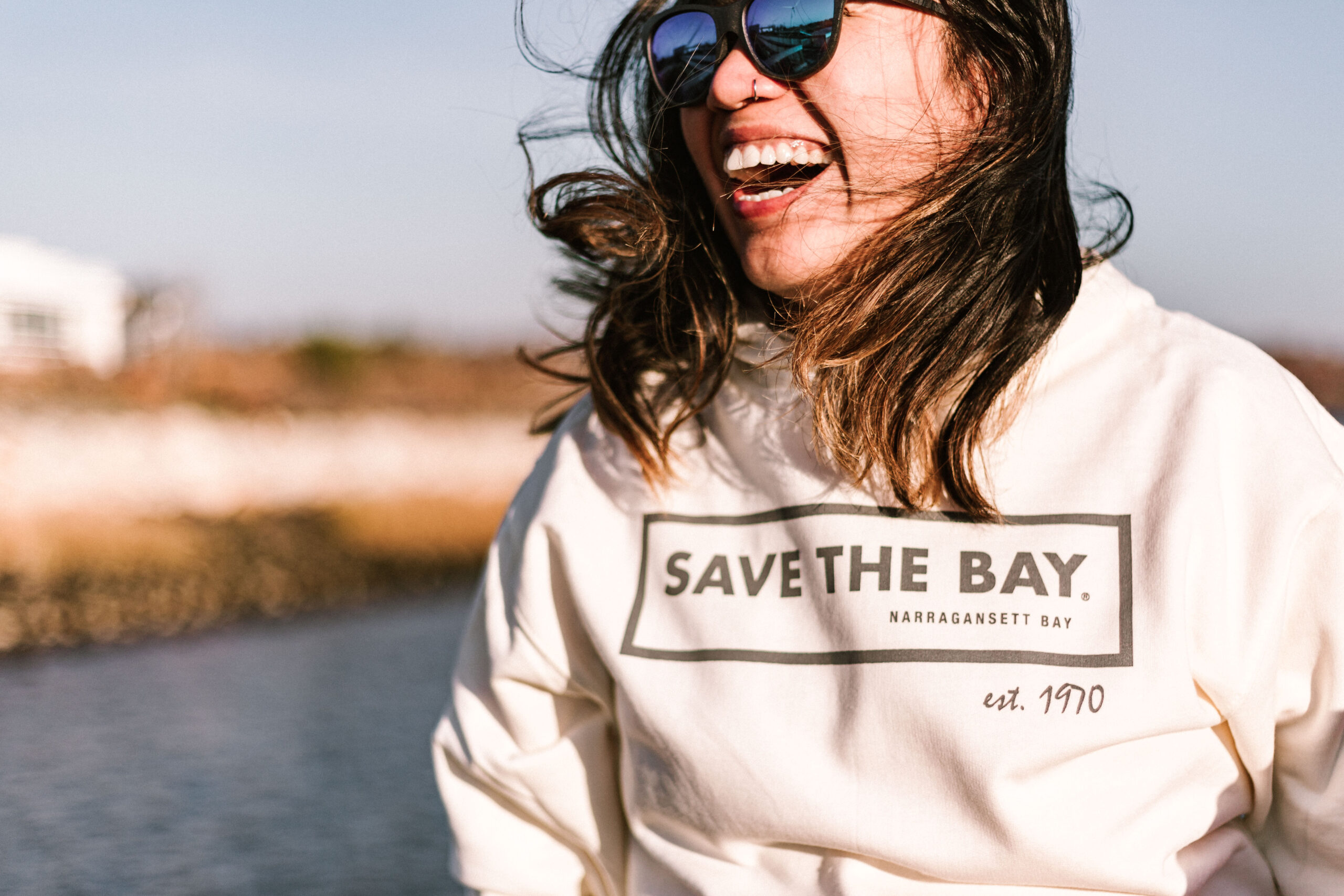 A Save The Bay staff member dons a cream colored hoodie featuring the classic Save The Bay logo across the chest.