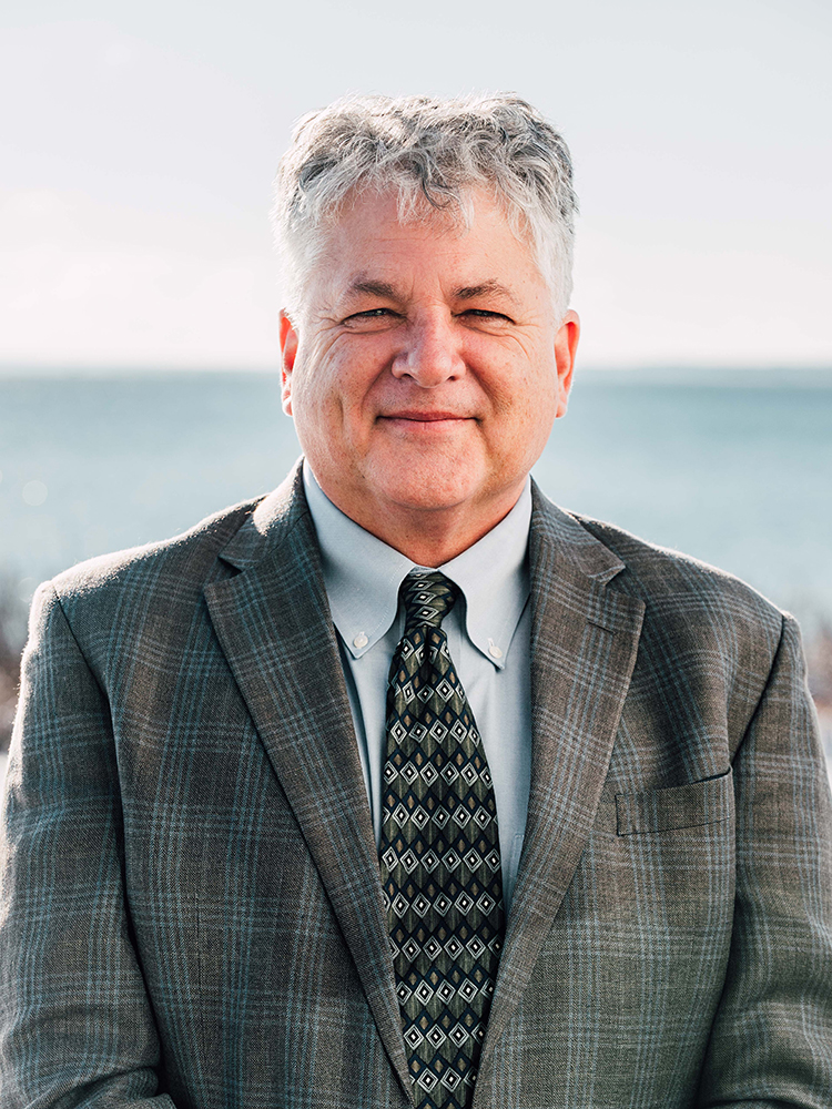 A headshot of Topher Hamblett, Save The Bay Executive Director, with the upper Narragansett Bay in the background