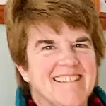 A photograph of Renay Houle in a teal zip up jacket and a buffalo plaid scarf.