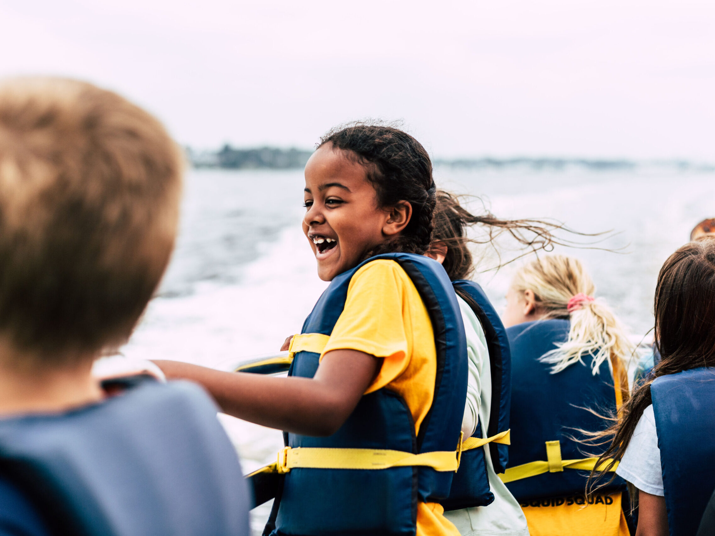 A BayCamper sporting a blue life jacket delights in a boat ride on Narragansett Bay in Summer 2023.