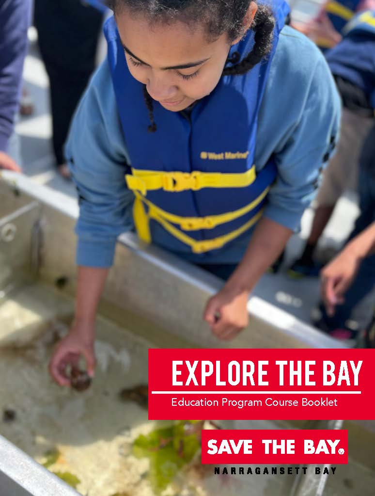 A student wearing a blue sweatshirt and a blue life jacket with yellow straps reaches into a shipboard tank to hold a small crustacean.